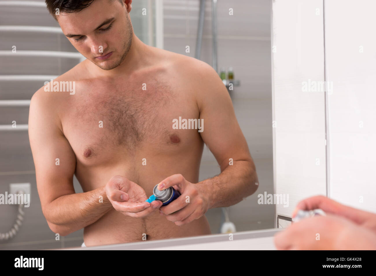 Le jeune homme de certains sur gel de rasage une main, debout devant un miroir dans la salle de bains moderne carrelée à la maison Banque D'Images