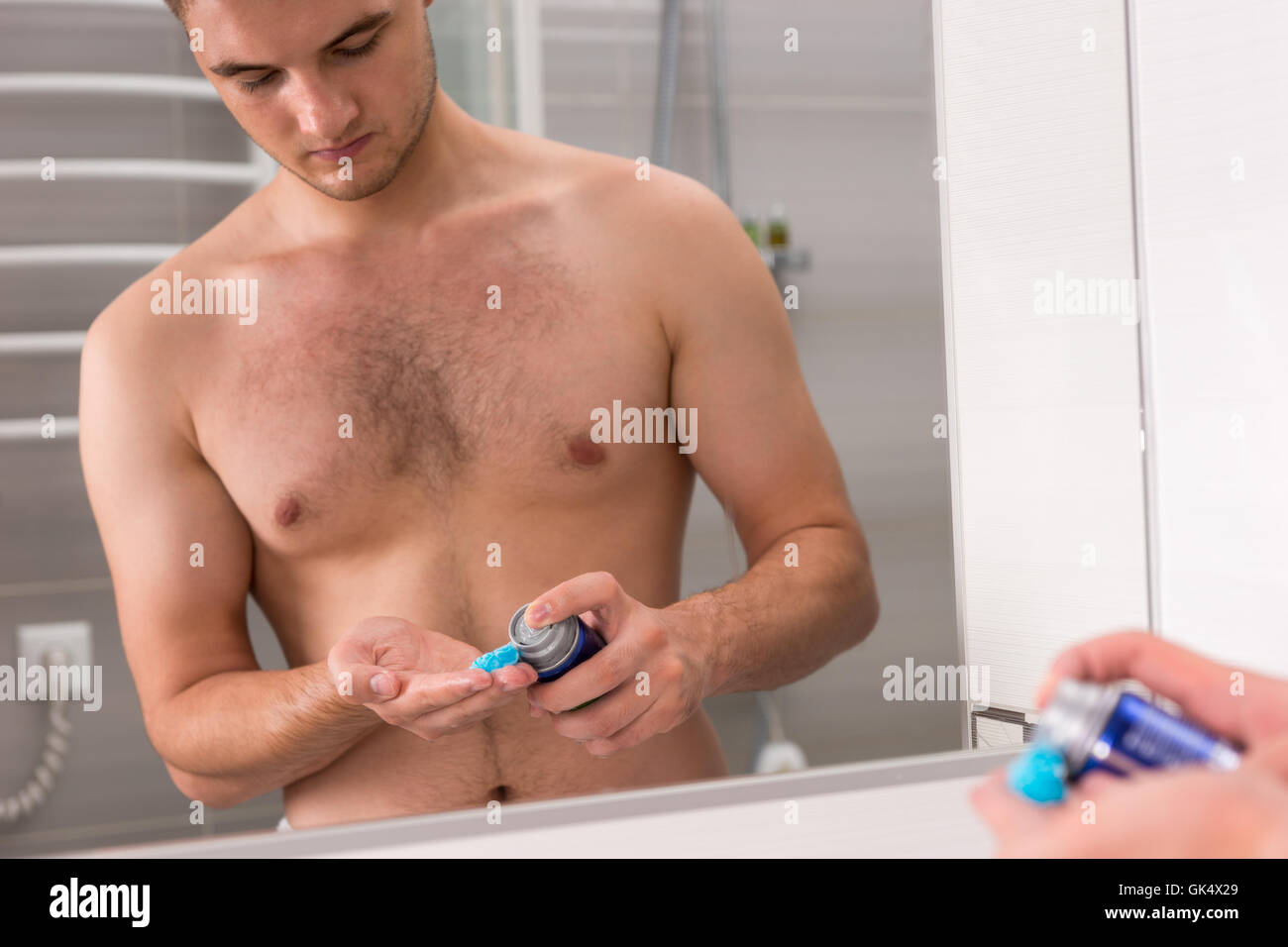 Mettre un peu de mâles sur gel de rasage une main, debout devant un miroir dans la salle de bains moderne carrelée à la maison Banque D'Images