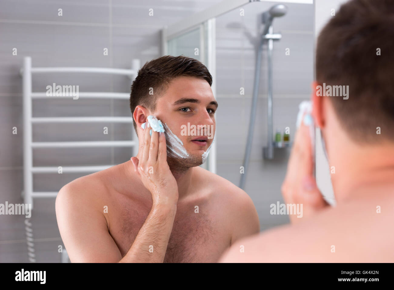 Guy enduit gel à raser sur son visage en face du miroir dans la salle de bains moderne carrelée à la maison Banque D'Images