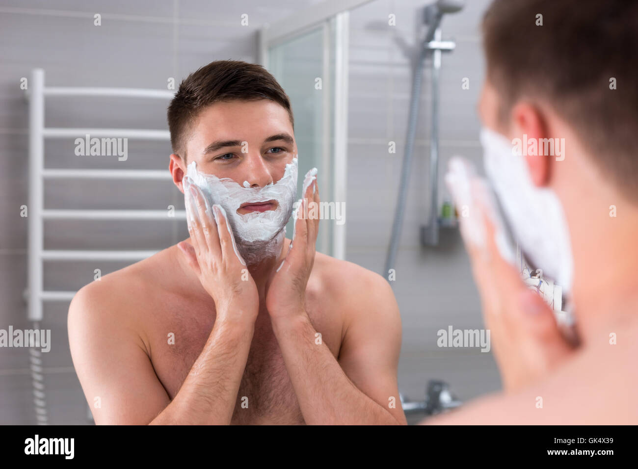 Bel homme enduit de gel de rasage sur le visage en face de miroir dans la salle de bains moderne carrelée à la maison Banque D'Images