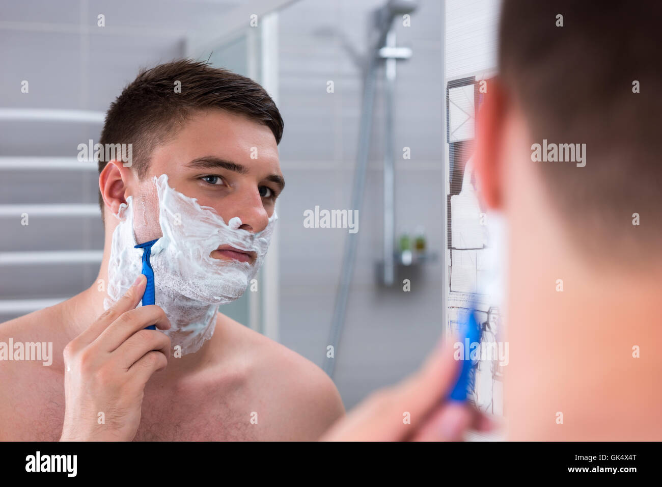 Jeune homme de son visage à la recherche et le miroir dans la salle de bains moderne carrelée à la maison Banque D'Images