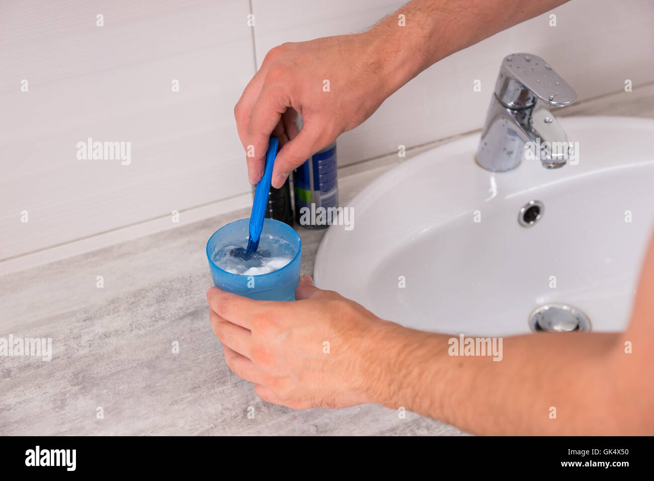 Laver les mains de l'homme un rasoir dans la tasse avec de l'eau près de lavabo dans la salle de bains moderne carrelée à la maison Banque D'Images