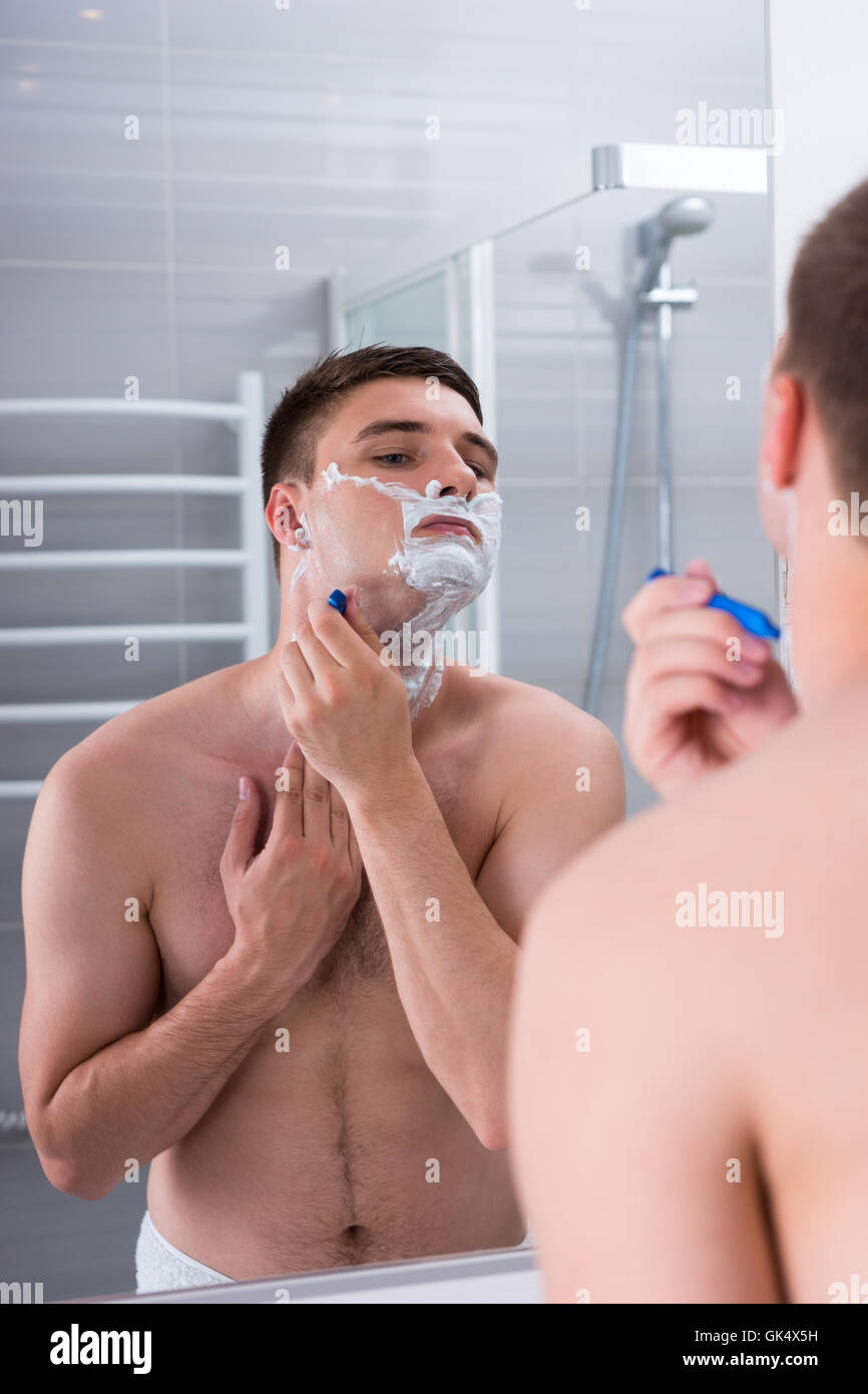 Rasage homme avec une razer et regardant le miroir dans la salle de bains moderne carrelée à la maison Banque D'Images
