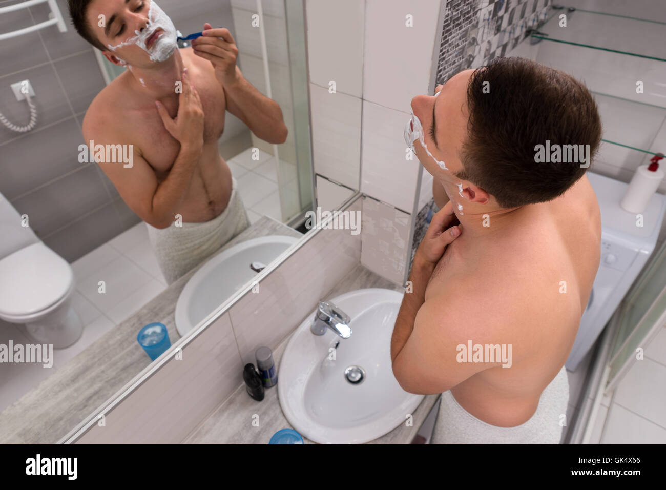 Bel homme de poitrine debout devant le miroir avec lavabo dans la salle de bains moderne carrelée à la maison Banque D'Images