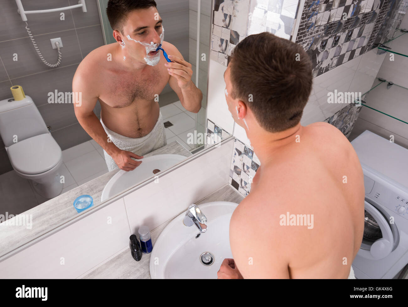 Vue de dessus sur un rasage homme debout devant le miroir avec lavabo dans la salle de bains moderne carrelée à la maison Banque D'Images