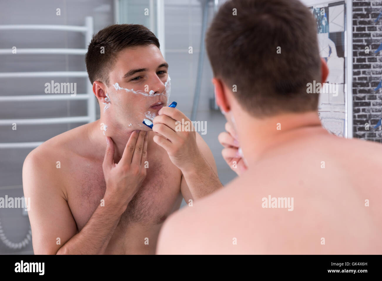 Rasage homme concentré avec un razer et regardant le miroir dans la salle de bains moderne carrelée à la maison Banque D'Images