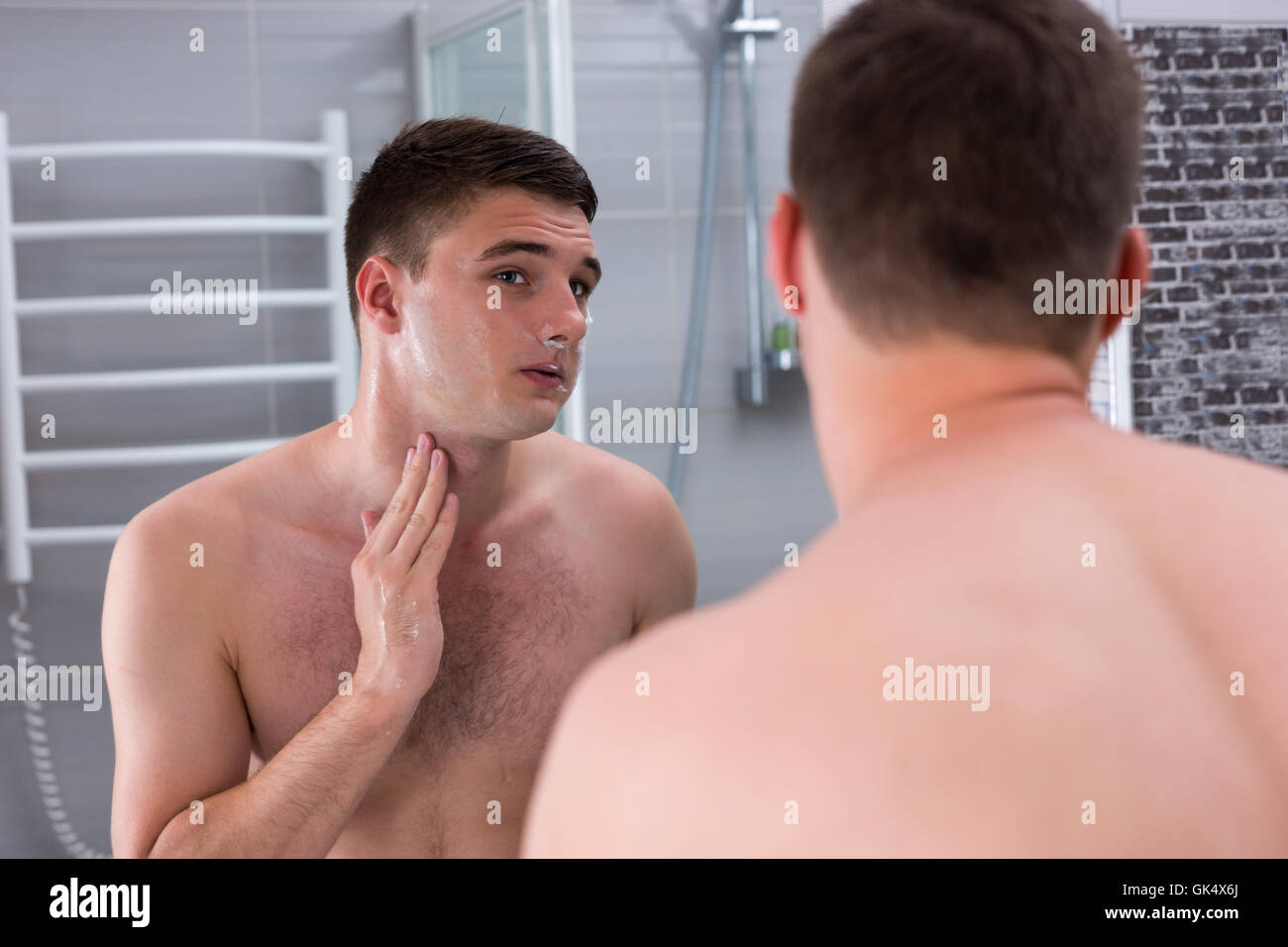 Jeune homme séduisant après le rasage à la recherche dans le miroir dans la salle de bains moderne carrelée à la maison Banque D'Images