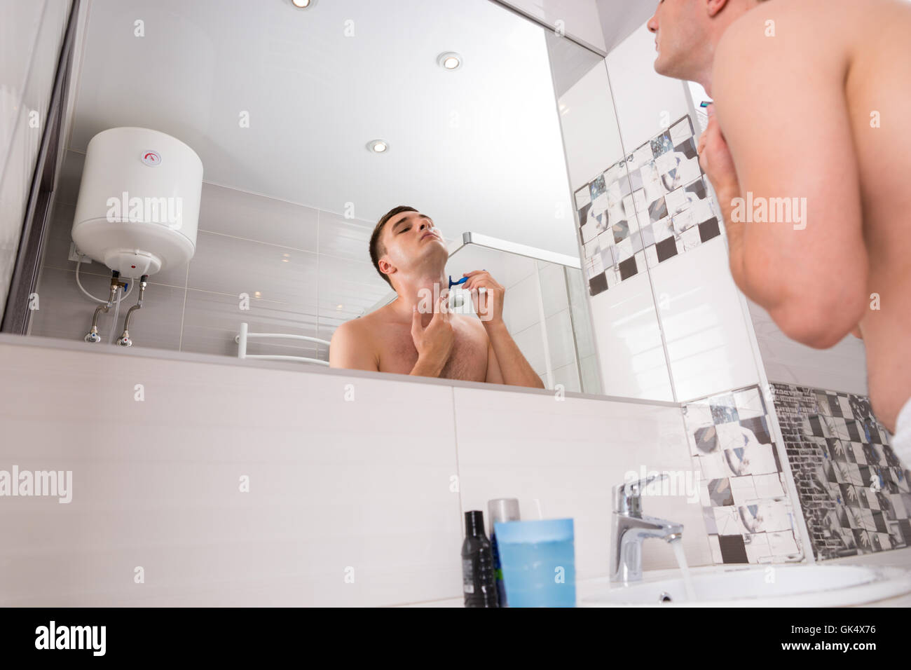 Vue de dessous du bel homme de son visage se tenait devant le miroir avec lavabo dans la salle de bains moderne carrelée à la maison Banque D'Images