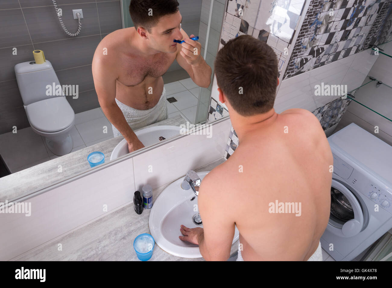 Vue de dessus sur un jeune homme le rasage d'une razer debout devant le miroir avec lavabo dans la salle de bains moderne carrelée à Banque D'Images