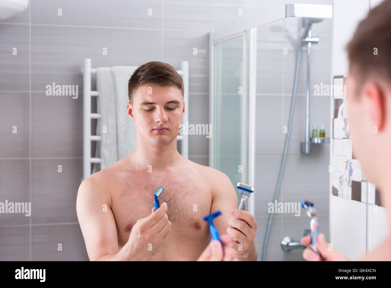 Man holding rasoirs et choisit le meilleur alors qu'il se tenait devant le miroir de la salle de bains moderne carrelée à la maison Banque D'Images
