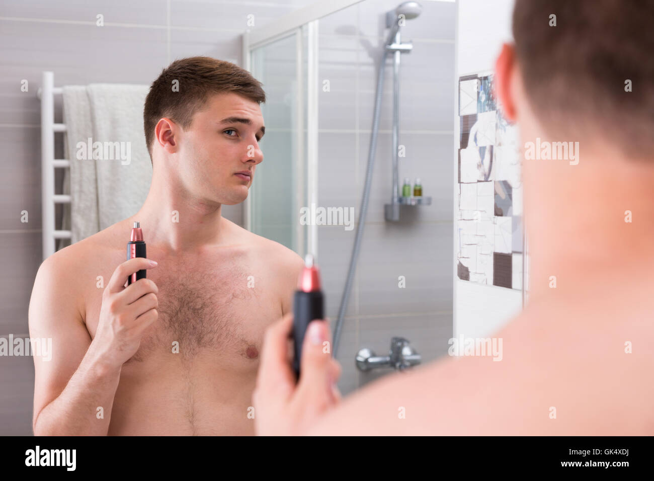 Homme tenant une tondeuse alors qu'il se tenait devant le miroir de la salle de bains moderne carrelée à la maison Banque D'Images
