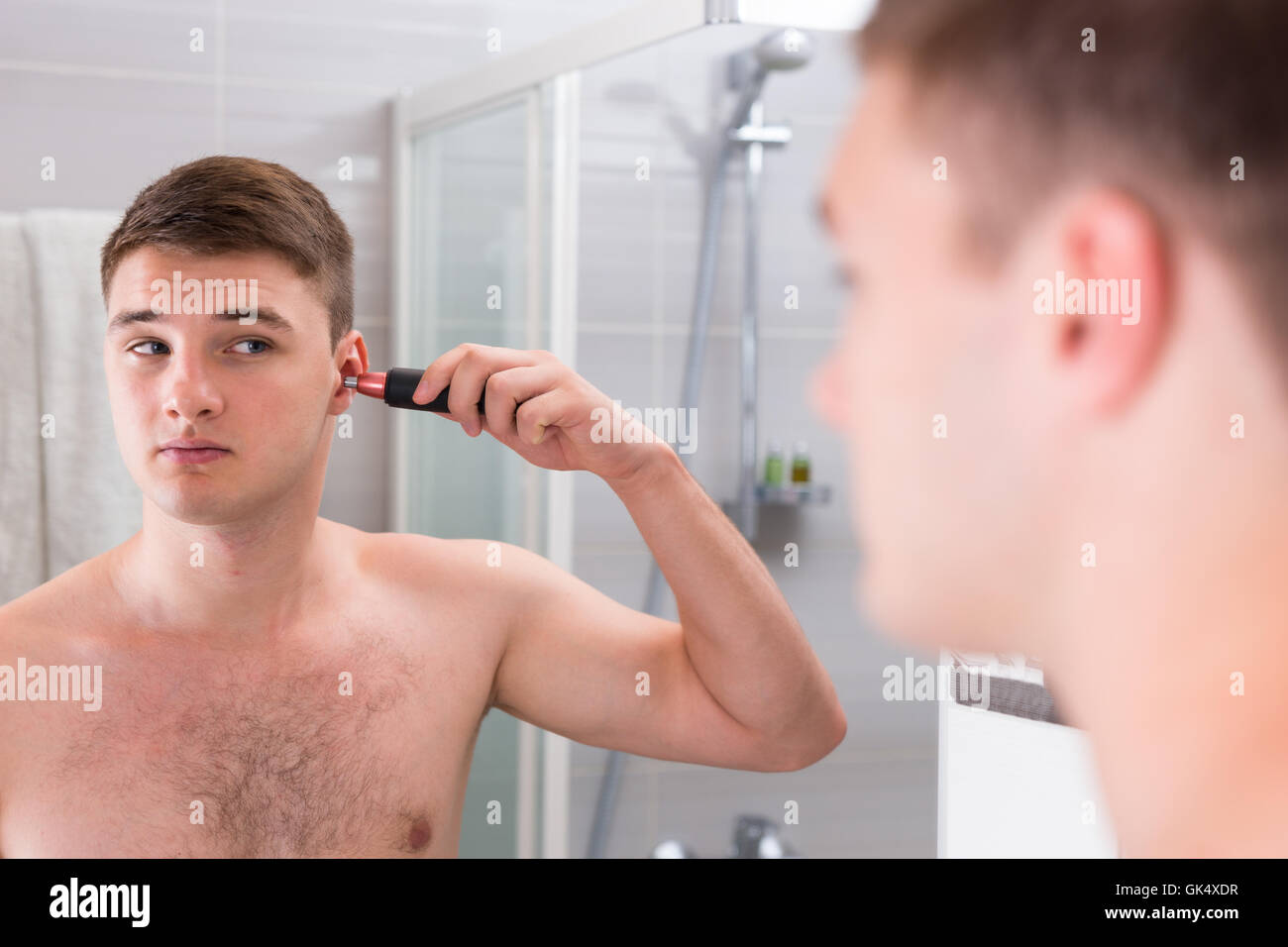Bel homme de son oreille au debout devant le miroir dans la salle de bains moderne carrelée à la maison Banque D'Images