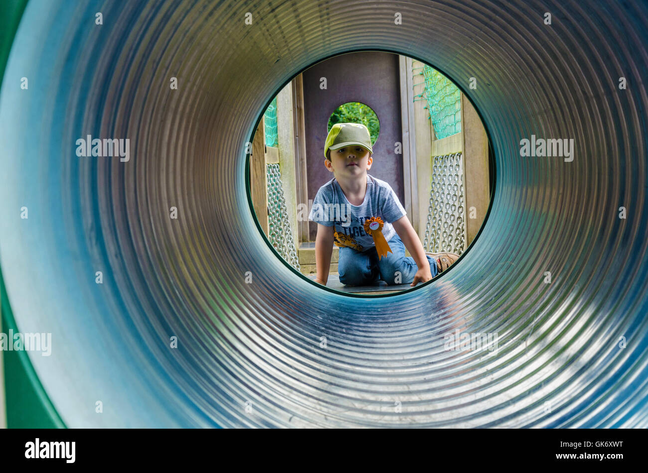 Un jeune garçon regarde à travers un tunnel dans une aire de jeux pour enfants. Banque D'Images