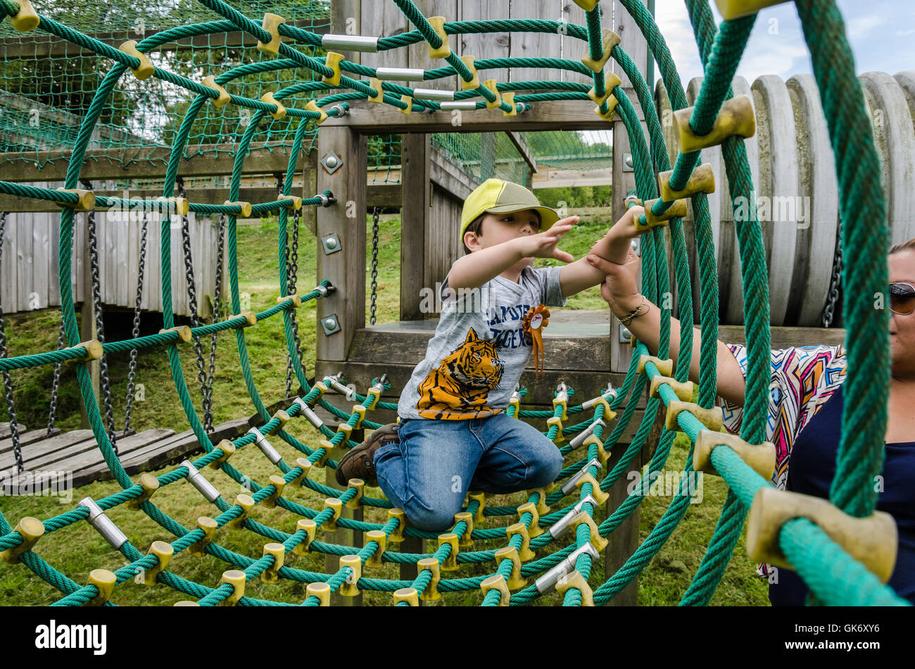 Un jeune garçon joue sur une nette escalade à une aire de jeux pour enfants avec un coup de main de sa maman. Banque D'Images
