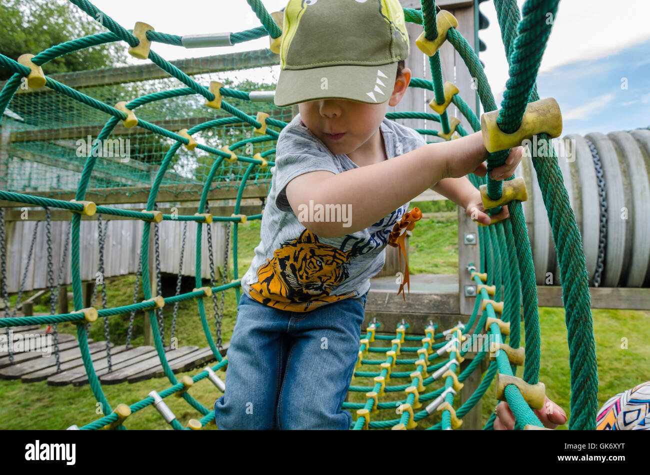 Un jeune garçon joue sur une nette escalade à une aire de jeux pour enfants avec un coup de main de sa maman. Banque D'Images
