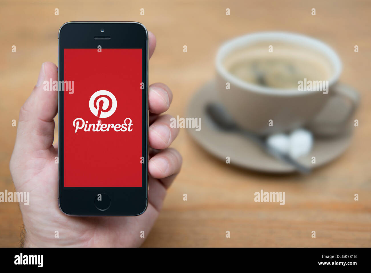 Un homme se penche sur son iPhone qui affiche le logo Pinterest, tandis qu'assis avec une tasse de café (usage éditorial uniquement). Banque D'Images