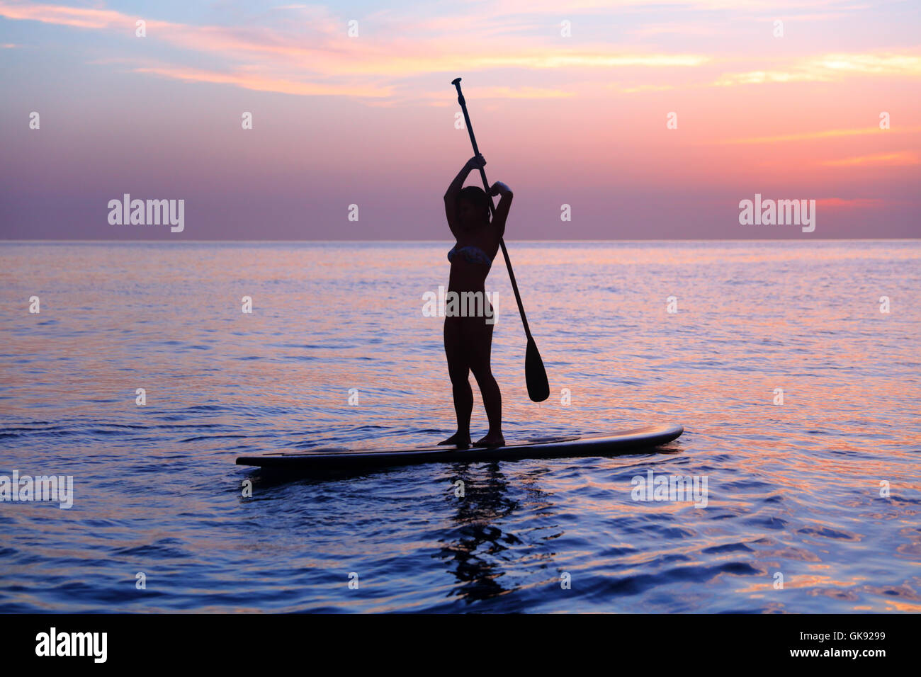Silhouette d'une jeune fille pratiquant, en équilibre sur SUP paddle board dans la mer sur la magnifique coucher de soleil violet, mode de vie sain Banque D'Images