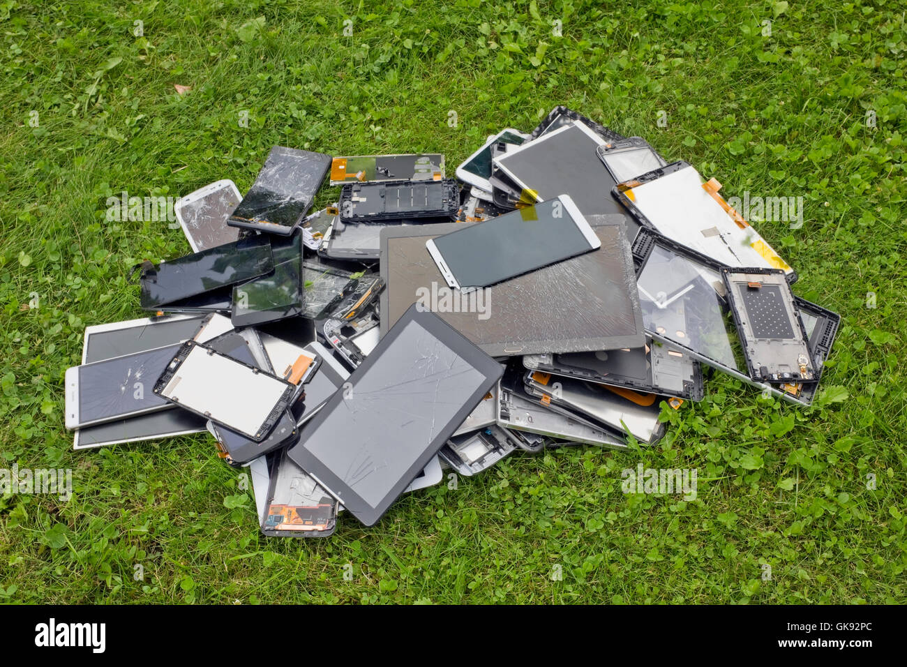 Gros tas de la casse et craquelée telephons cellulaires et tablettes se trouvent sur pelouse verte de l'herbe. Les technologies modernes polluent enviro Banque D'Images