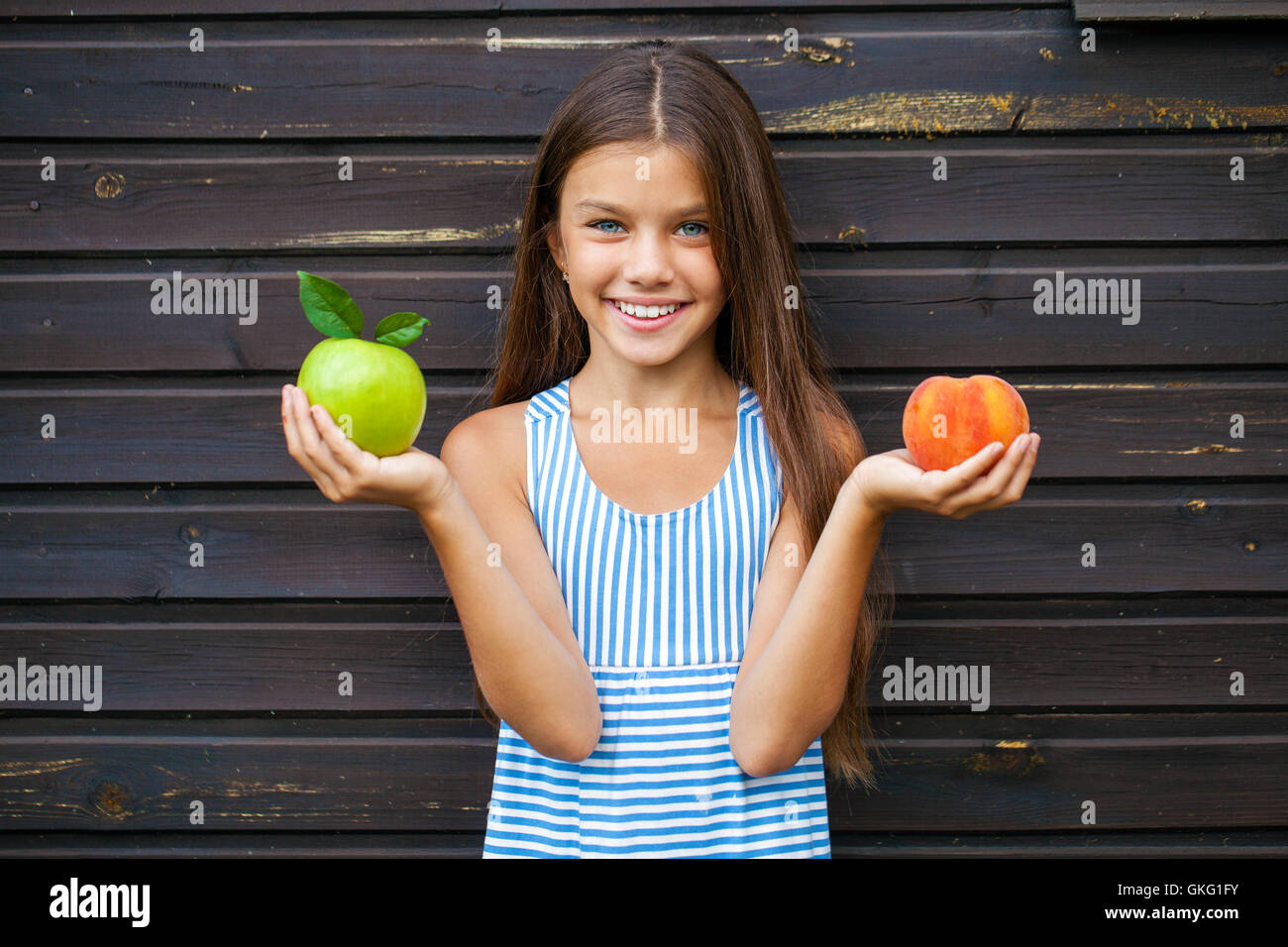 Petite fille tenant une pomme verte et une pêche, plein air d'été Banque D'Images