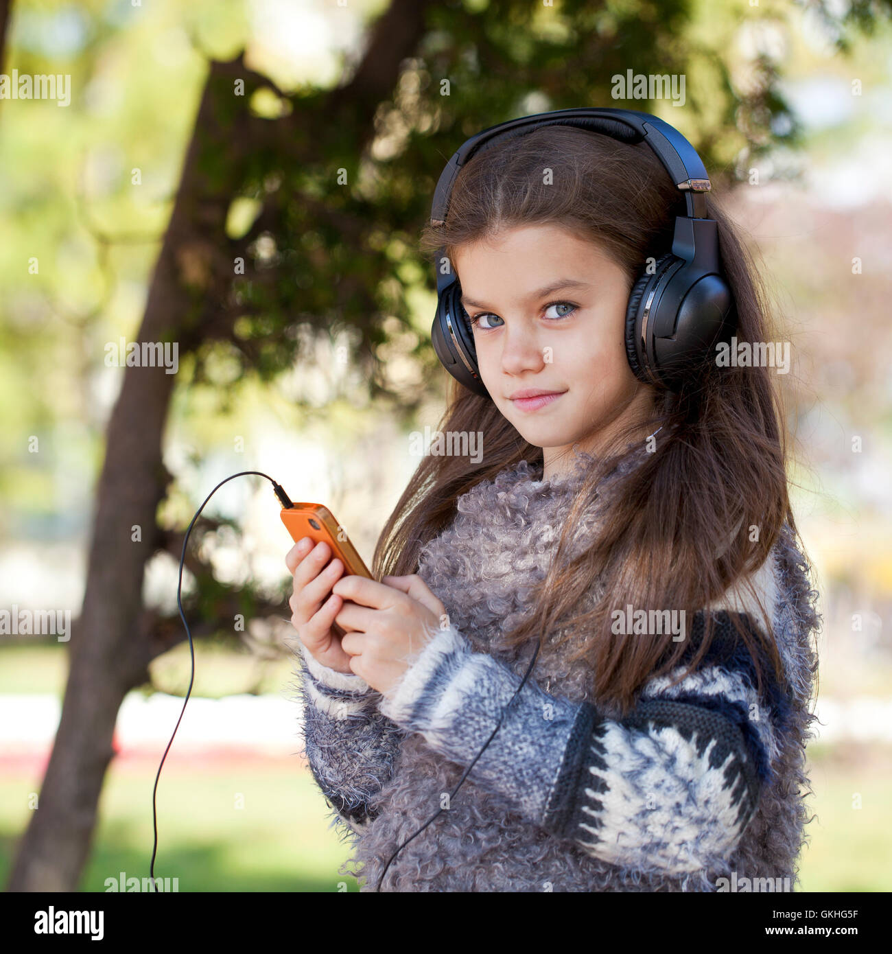 Belle petite fille listening to music on headphones in autumn park Banque D'Images
