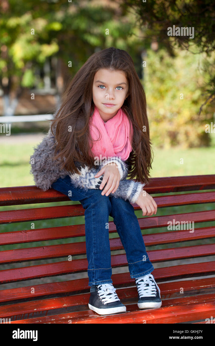 Belle petite fille assise sur un banc dans le parc en automne Banque D'Images