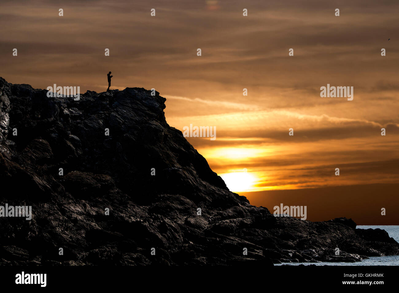 Homme marchant le long d'une falaise à Porth Dafarch, Anglesey, consulte une carte au coucher du soleil Banque D'Images