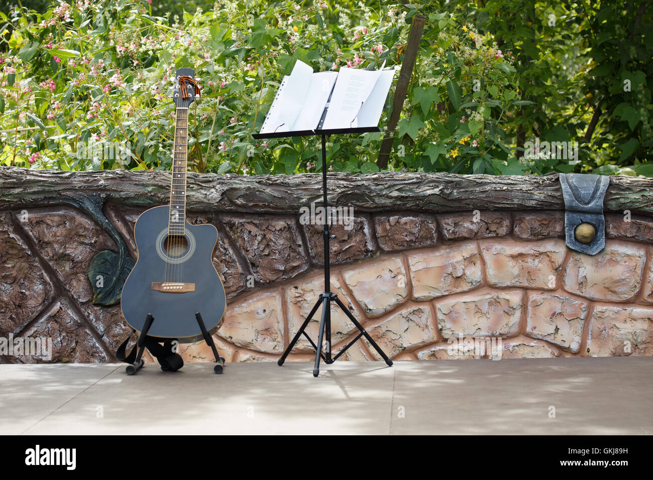Encore de concert. Guitare acoustique debout sur la scène ouverte près de la clôture. Derrière la grille d'un jardin. Banque D'Images