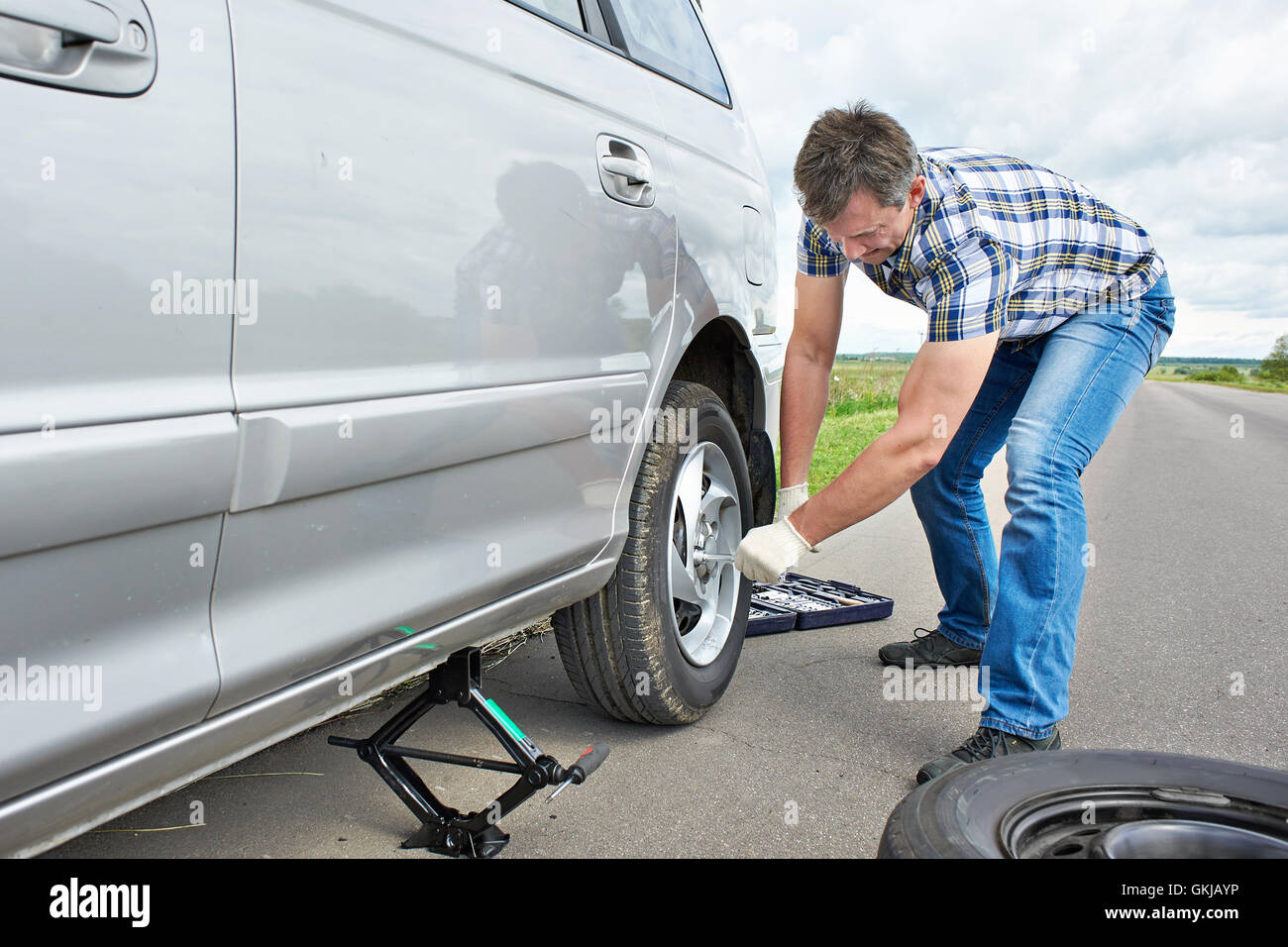 Homme avec jack changer un pneu de rechange de voiture sur route Banque D'Images