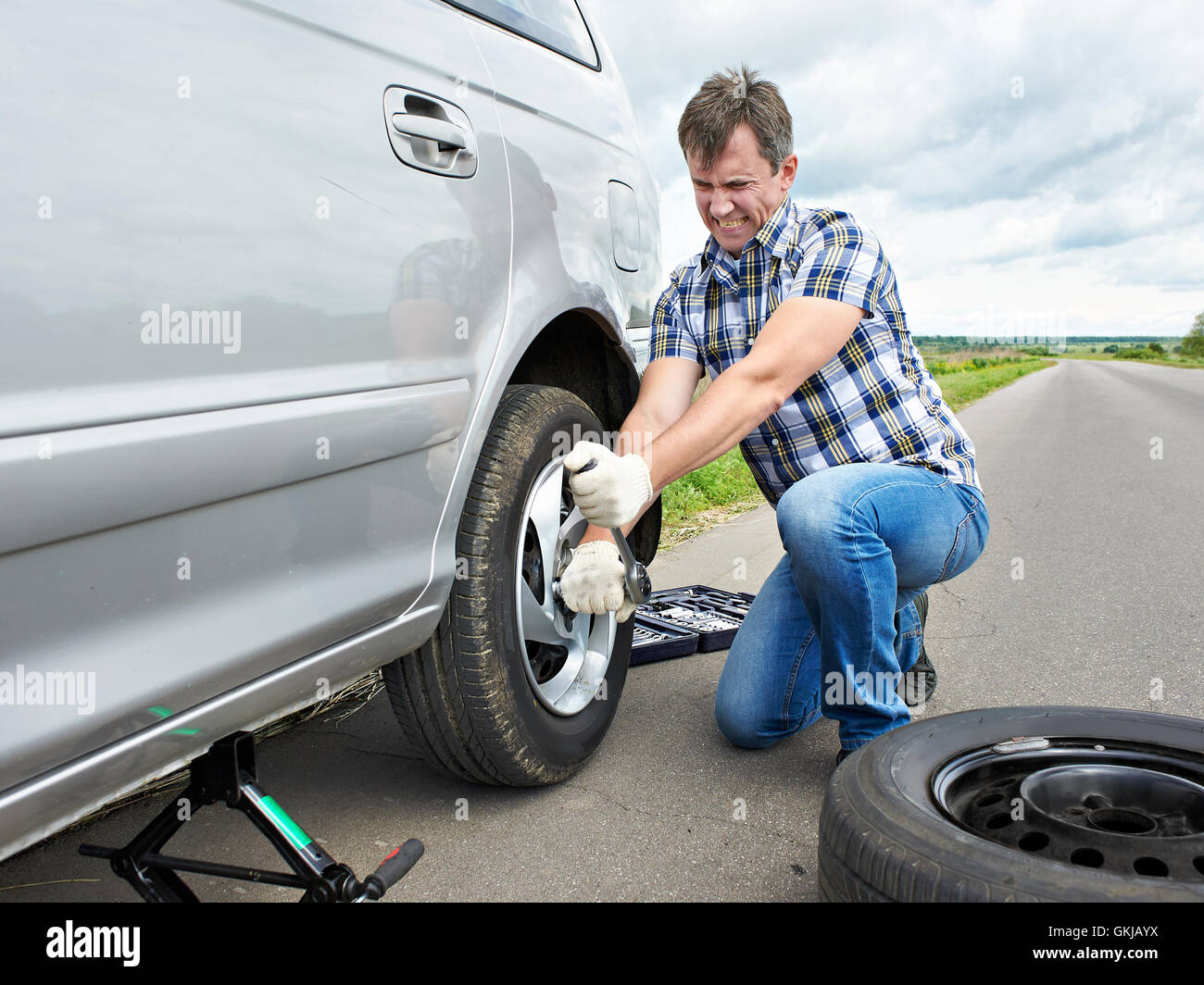 Homme avec jack changer un pneu de rechange de voiture sur route Banque D'Images