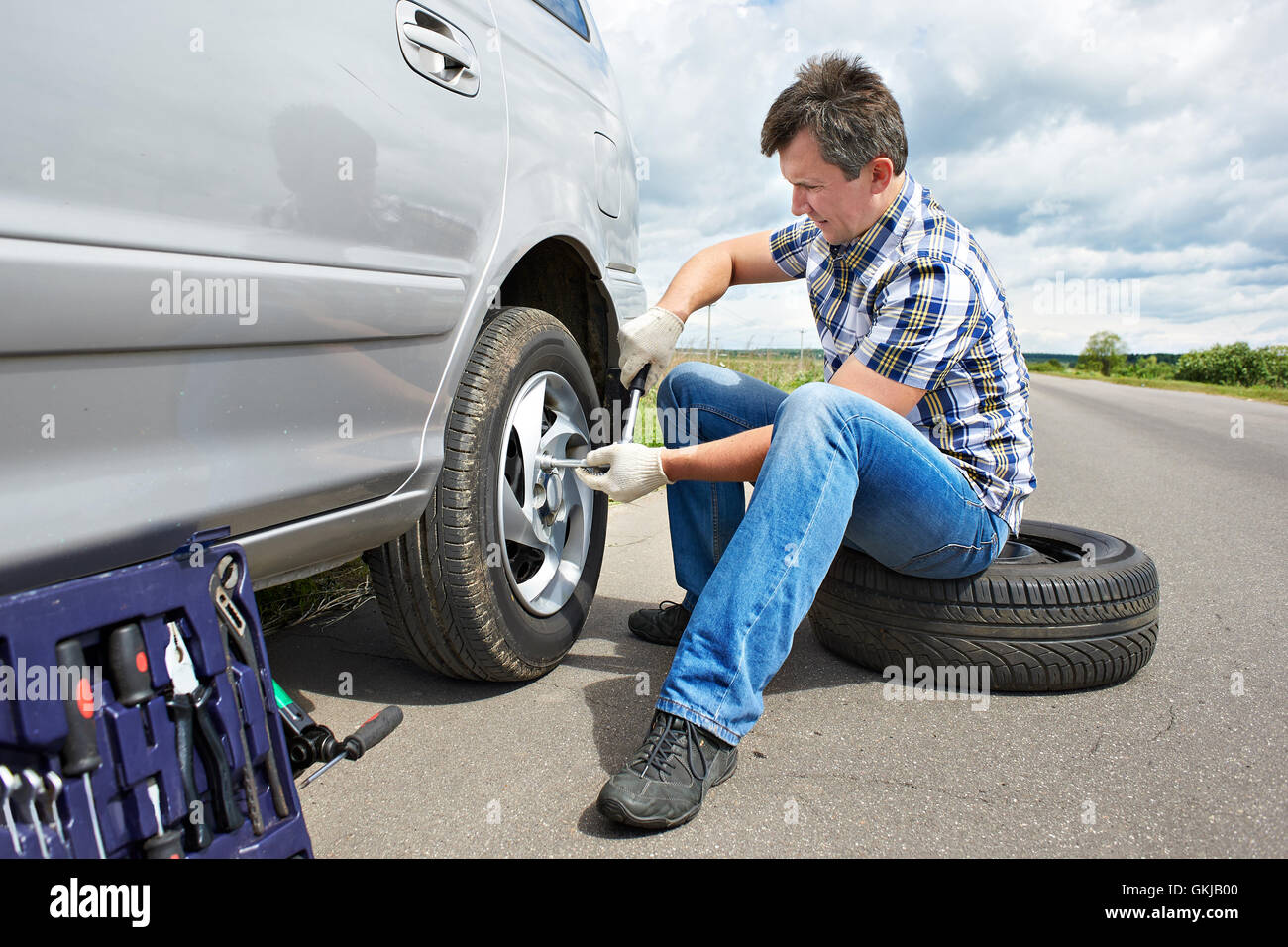 Homme avec jack changer un pneu de rechange de voiture sur route Banque D'Images