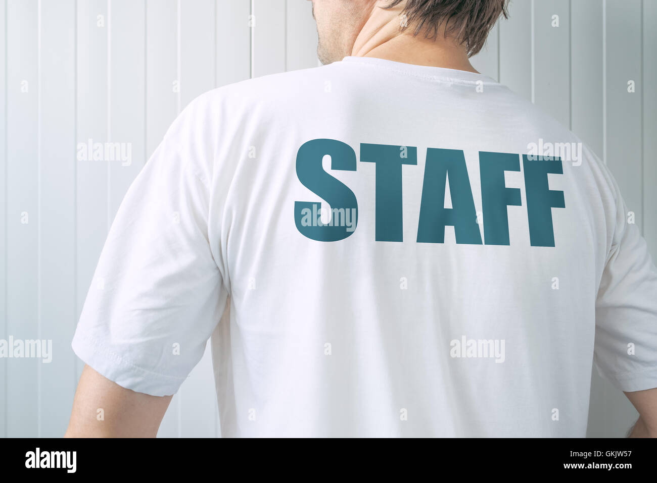 Homme portant un t-shirt blanc avec le personnel du titre à l'arrière, membre de l'équipe des employés face au mur Banque D'Images