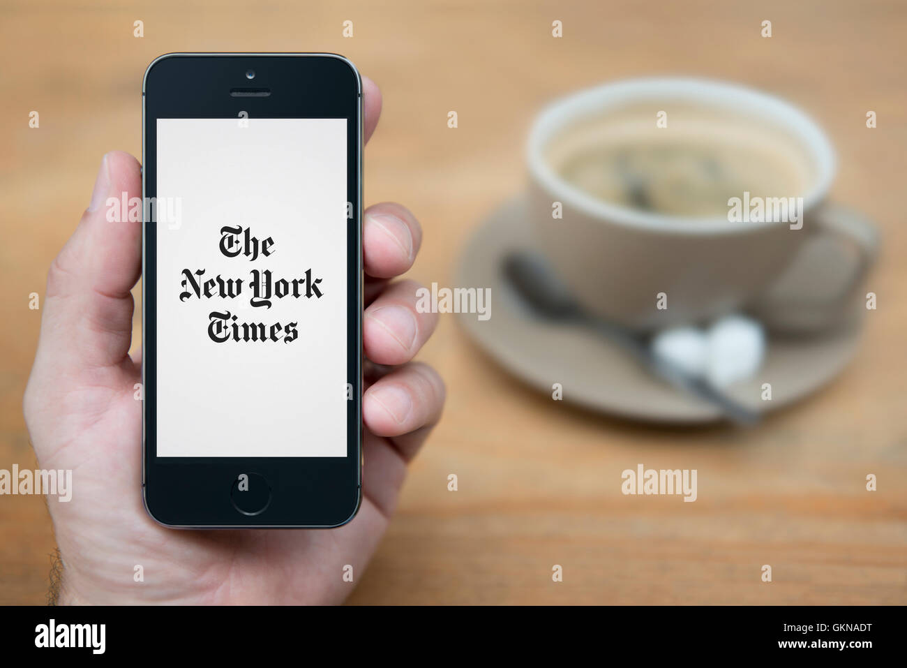 Un homme se penche sur son iPhone qui affiche le logo du New York Times, alors qu'assis avec une tasse de café (usage éditorial uniquement). Banque D'Images