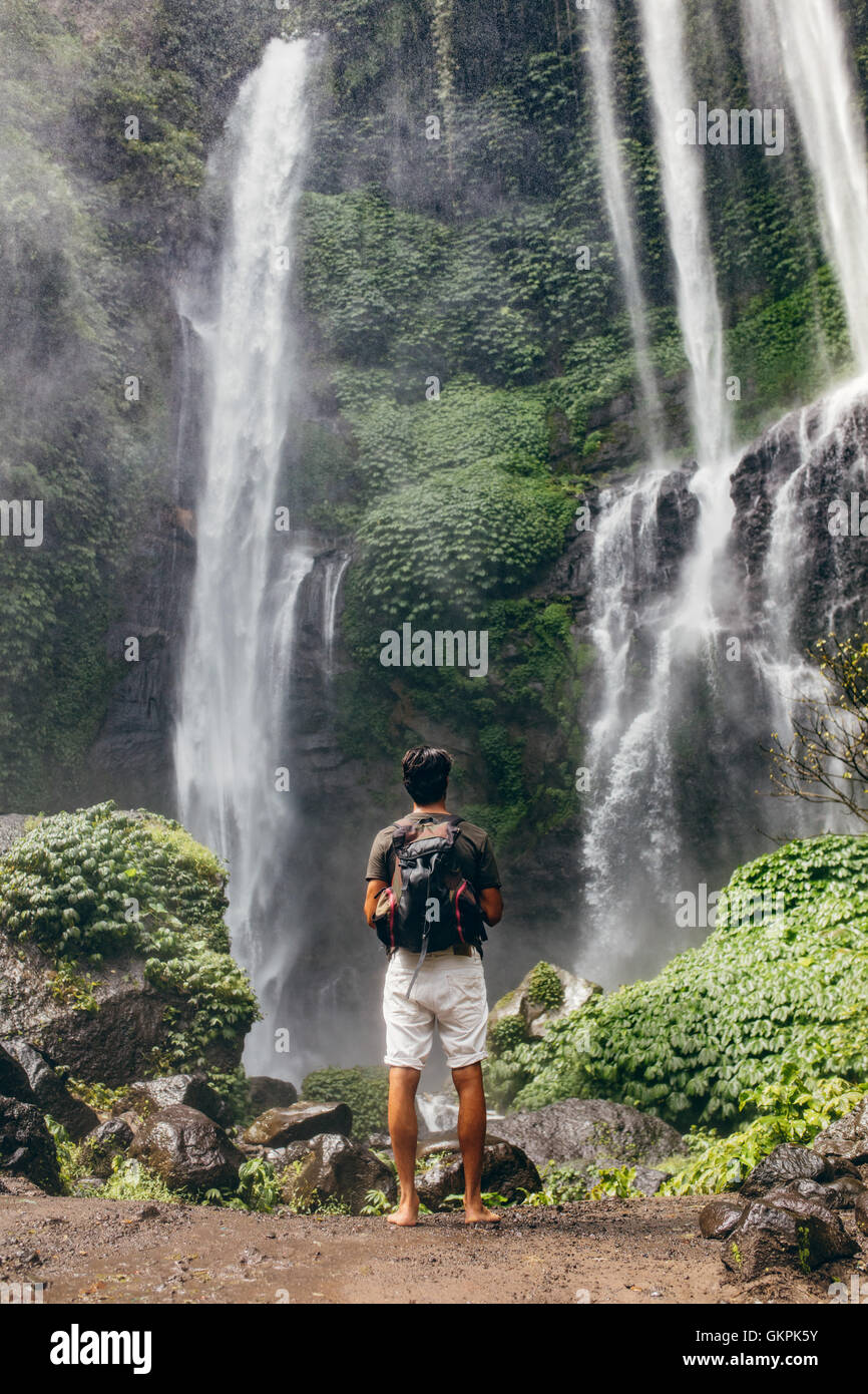 Longueur totale shot of young male hiker looking at waterfall. Vue arrière du jeune homme avec sac à dos, debout près de cascade de fores Banque D'Images