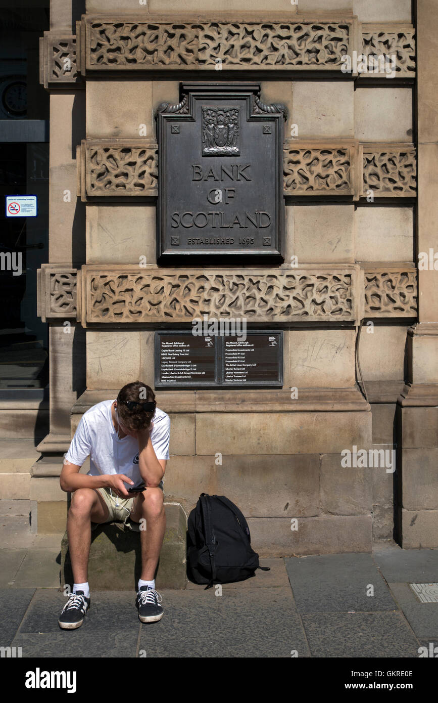 Un jeune homme vérifie son téléphone alors qu'il était assis à la porte de la Lloyds Banking Group siège écossais anciennement HBoS Banque D'Images