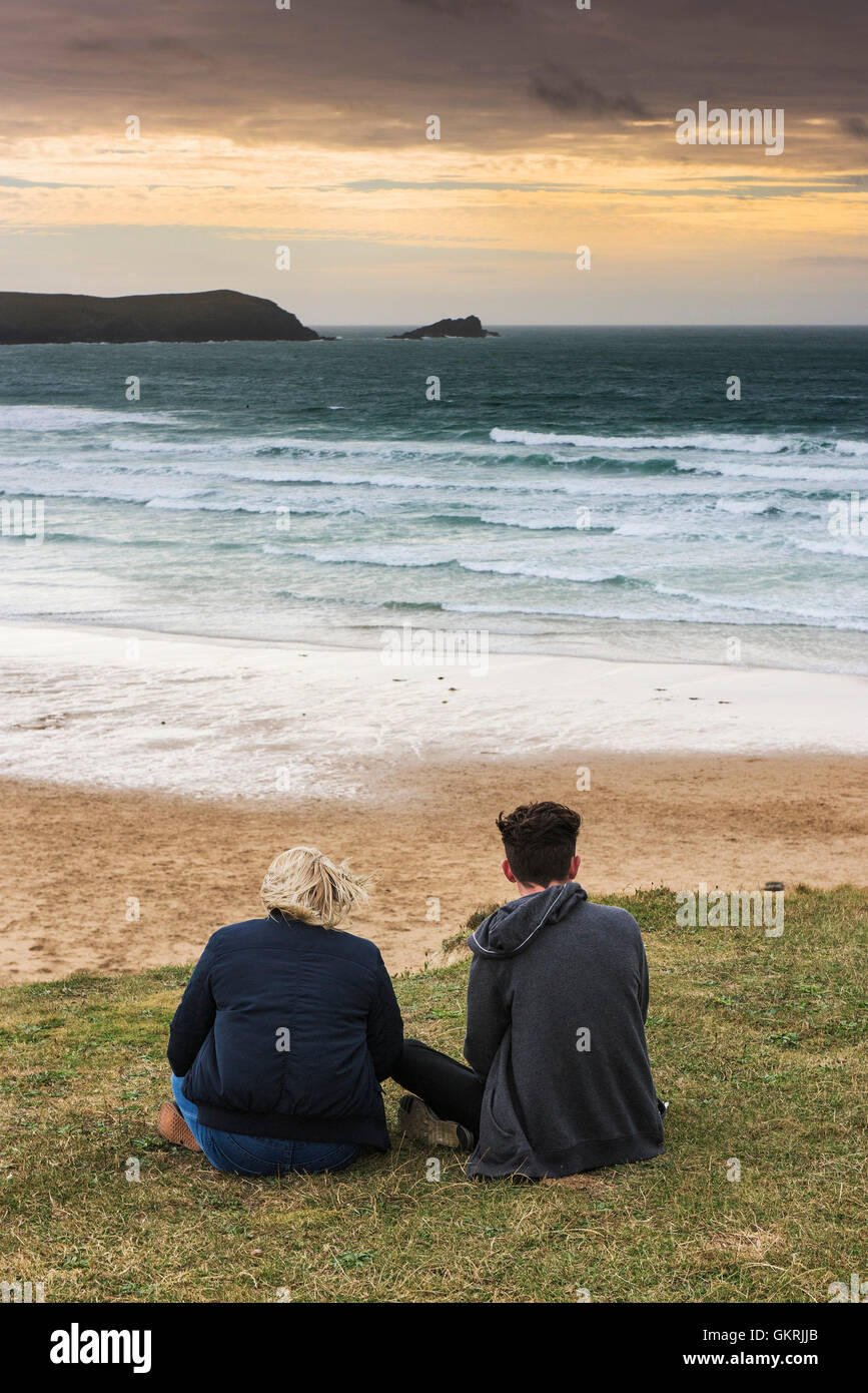 Deux adolescents assis surplombant la plage de Fistral pendant que le soleil commence à définir. Banque D'Images