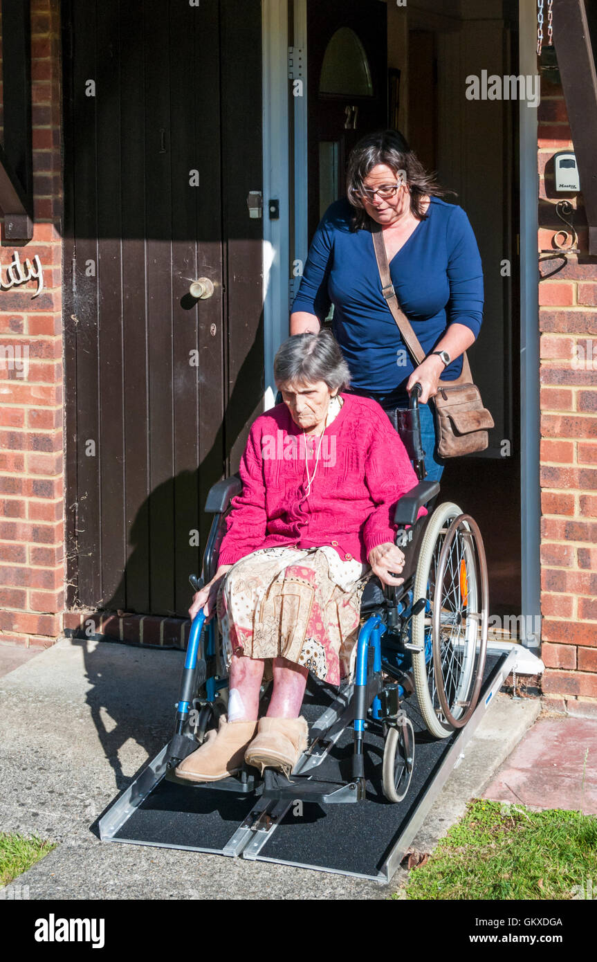 Une vieille dame de 96 ans quitte son abri dans son fauteuil roulant par une rampe avec sa garde ou assistant. Banque D'Images