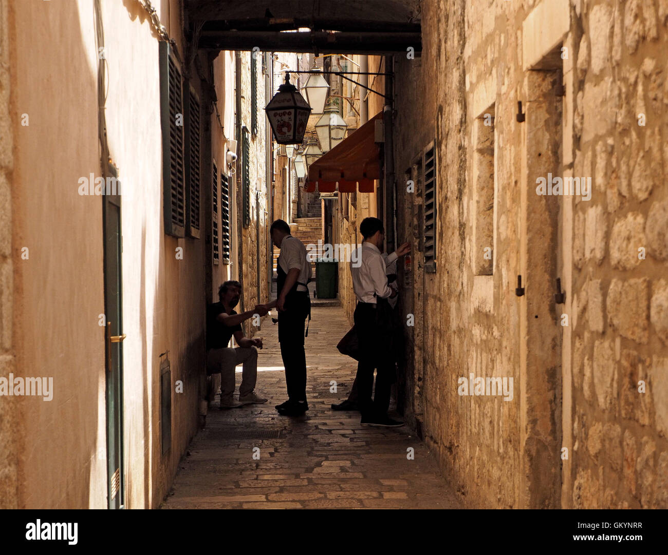 Les serveurs et le personnel de se serrer la main en guise de salutation ci-dessous lanterne dans la ruelle piétonne ombragée dans la vieille ville fortifiée de Dubrovnik, Croatie Banque D'Images