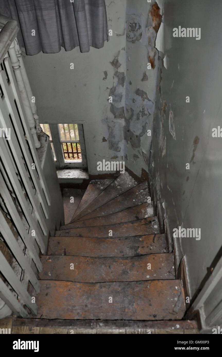Un escalier en bois de travers et de l'écaillage de la peinture mur dans maison abandonnée. Banque D'Images