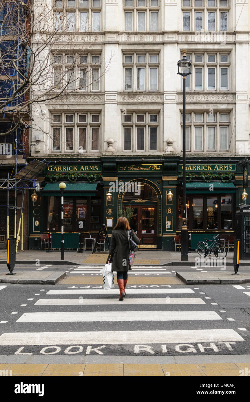 Femme marche sur passage pour piétons sur Charing Cross Road en direction de Garrick Arms pub, Londres. Banque D'Images