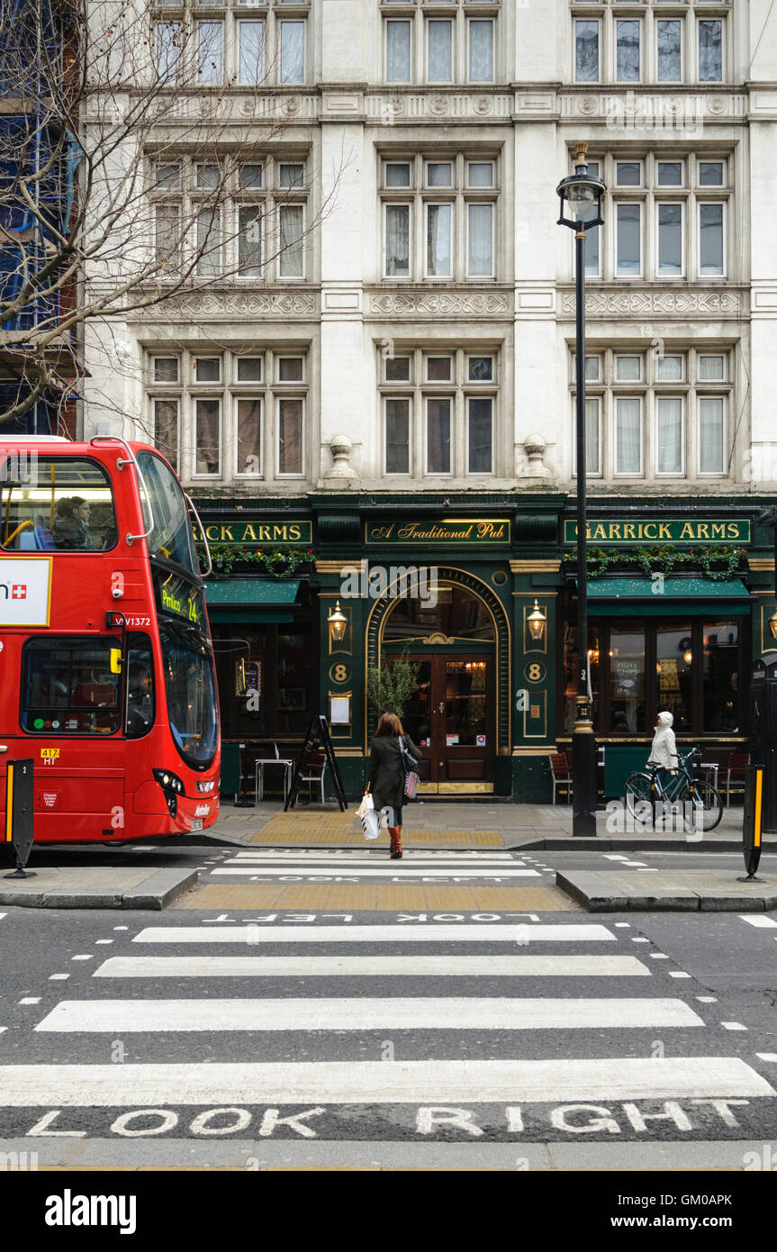 Femme marche sur passage pour piétons sur Charing Cross Road en direction de Garrick Arms pub, Londres. Banque D'Images