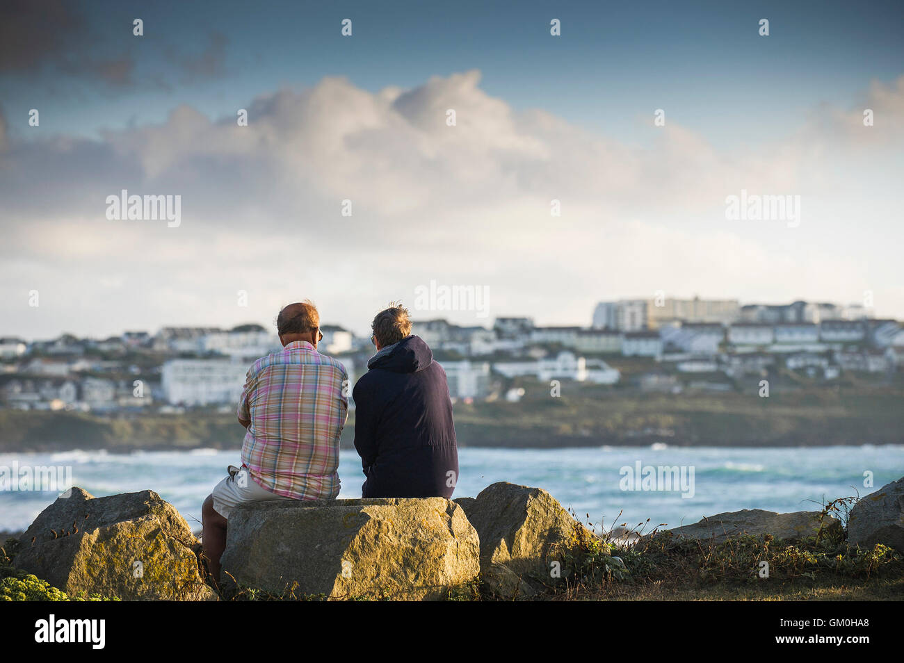 Deux vacanciers, s'asseoir sur des rochers surplombant dans Fistral Newquay, Cornwall. Banque D'Images