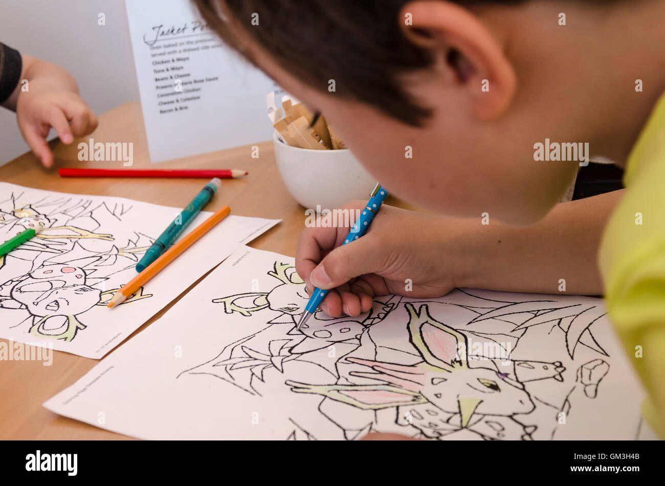 Un jeune garçon fait un peu de dessin et coloriage de dans un café en attendant que la nourriture d'arriver. Banque D'Images