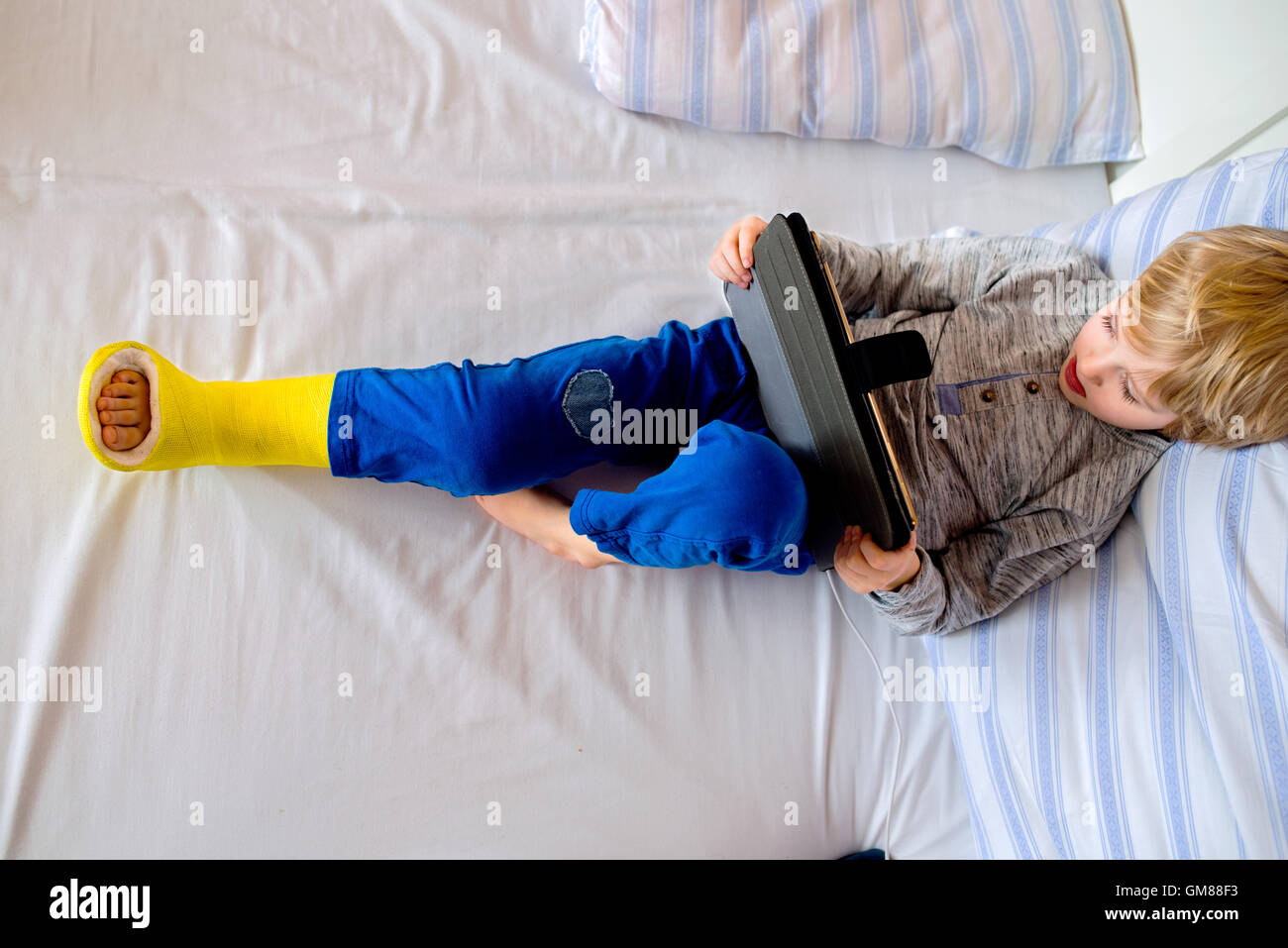 Petit garçon avec jambe cassée de jouer sur tablette Banque D'Images