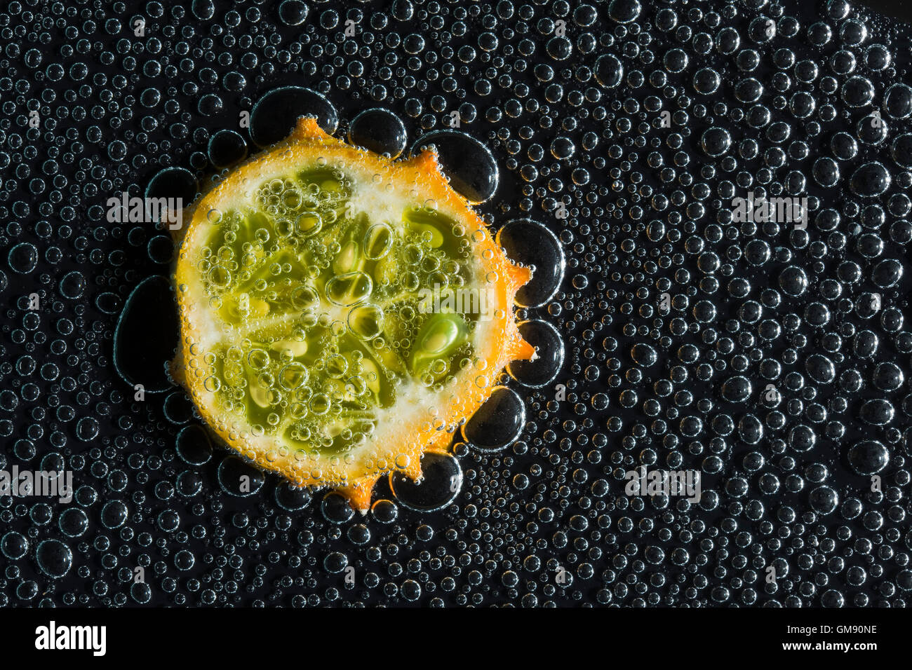 Kiwano fruit melon à cornes, dans l'eau minérale, une série de photos. Close-up de l'eau gazéifiée sur fond noir Banque D'Images
