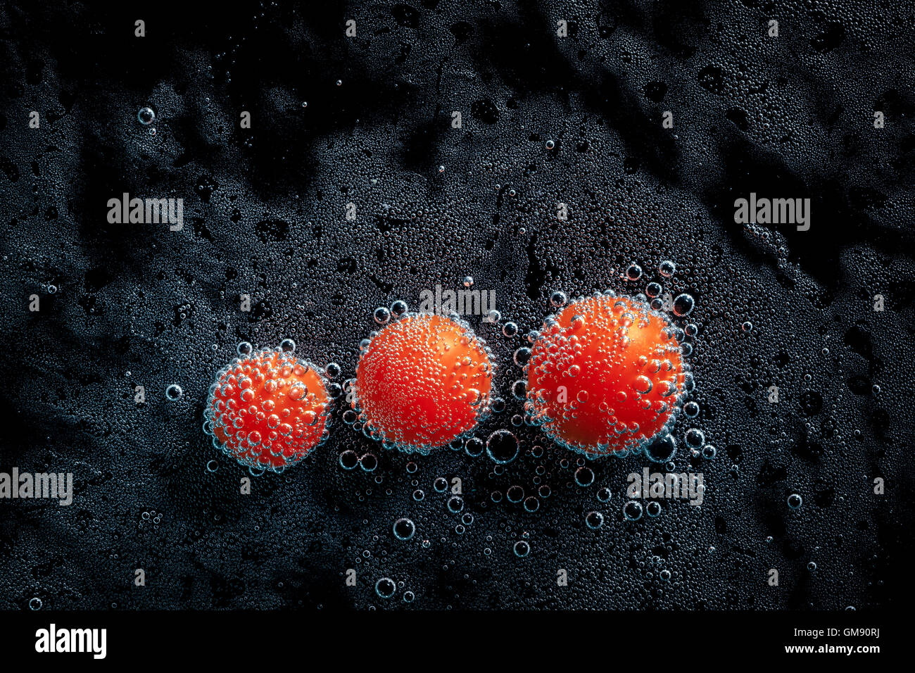 Tomates cerises dans de l'eau minérale, une série de photos. Close-up de l'eau gazéifiée sur fond noir, conceptuel Banque D'Images