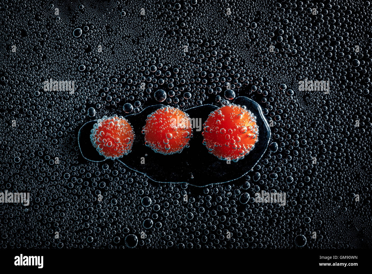 Tomates cerises dans de l'eau minérale, une série de photos. Close-up de l'eau gazéifiée sur fond noir, conceptuel Banque D'Images