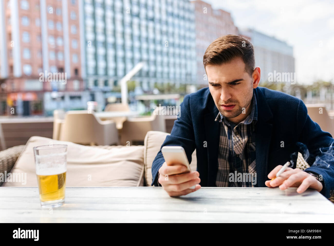 Jeune homme en attente à outdoor cafe looking at cell phone Banque D'Images