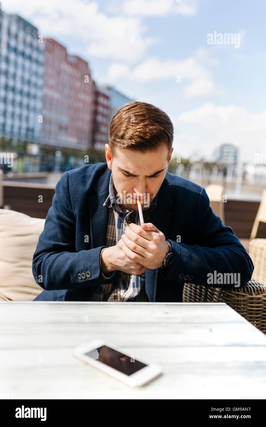 Jeune homme en attente à outdoor cafe allumer une cigarette Banque D'Images