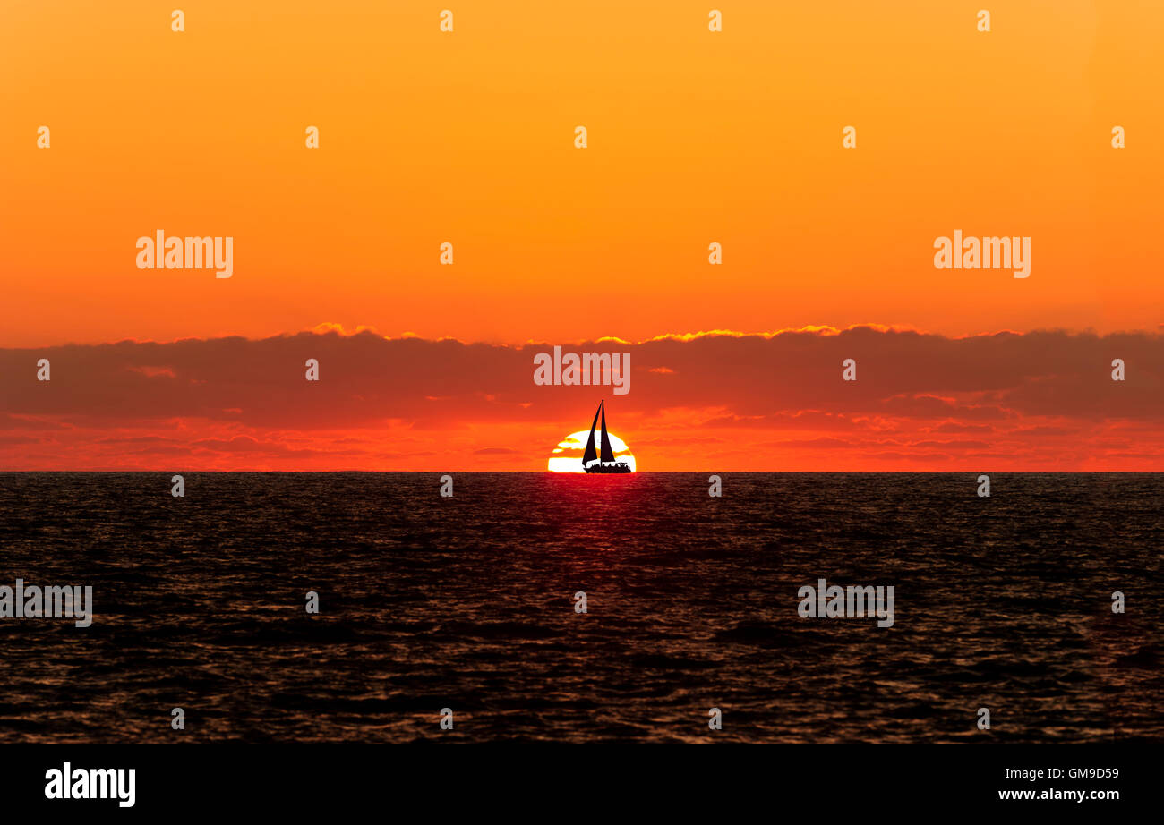Voilier sunset silhouette est un bateau naviguant en toute voiles dehors silhouetted against a white réglage chaud soleil et orange vif Banque D'Images
