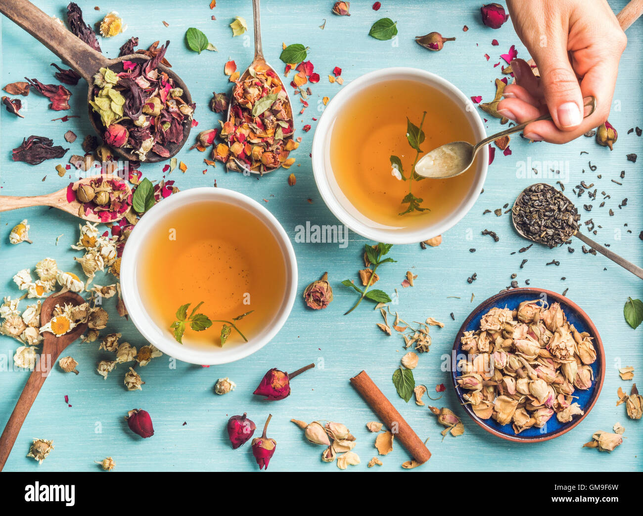 Deux tasses de thé à base de plantes en bonne santé avec la menthe, cannelle, rose, fleurs de camomille séchées dans des cuillères et man's hand holding spoon Banque D'Images